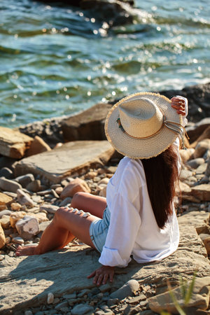 Mature woman resting on coastal rocks in sunlightの写真素材