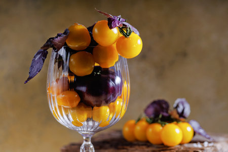 Rustic still life of yellow cherry tomatoes and purple basil in glassの写真素材
