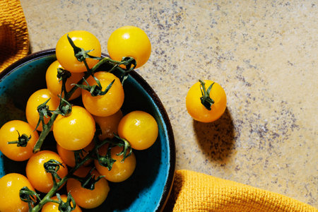Bowl of yellow cherry tomatoes on rustic stone surface with yellow fabricの写真素材