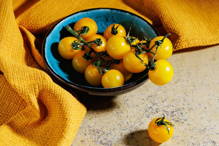 Yellow cherry tomatoes in blue bowl on yellow fabric with moody lightの写真素材
