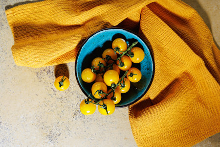 Top view of yellow cherry tomatoes in rustic blue bowl on yellow towelの写真素材