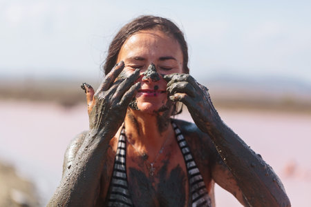 Woman applying mud to nose and cheeks with eyes closedの写真素材