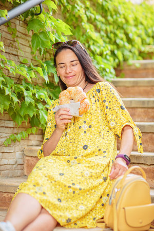 Attractive brunette woman sitting on stairs with bagelの写真素材