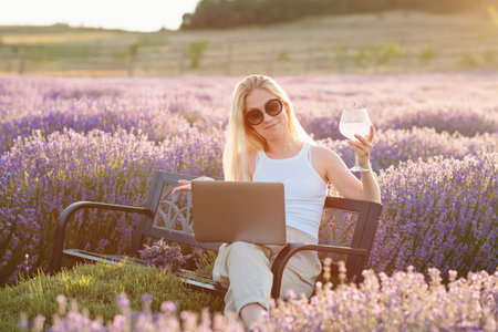 Woman sitting on bench among lavender flowers and working on laptop computerの写真素材