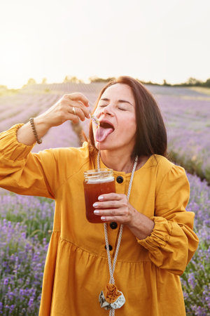 Mature woman tasting lavender honey from flower sprigの写真素材