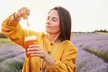 Woman lifting lavender flower with dripping honey in fieldの写真素材