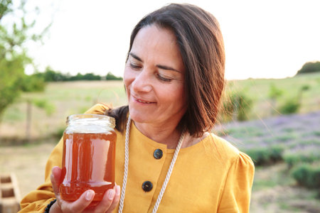 Woman admiring jar of honey in lavender fieldの写真素材