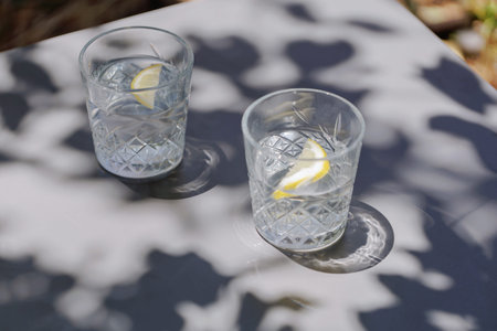 Two crystal glasses with lemon water on sunlit outdoor tableの写真素材