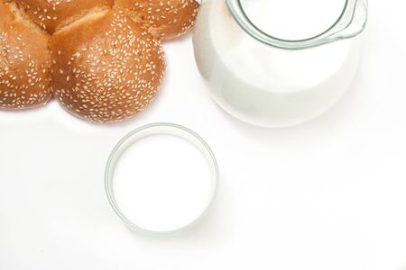 Milk in a glass jug, cup and bun on a white backgroundの写真素材