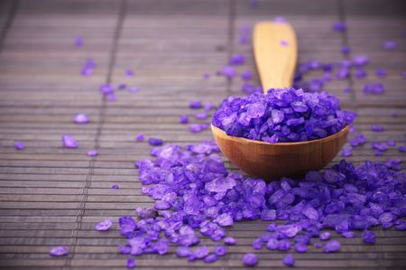 Violet bath salt in wooden spoon on brown mat. Violet bath salt in wooden spoon on brown mat.