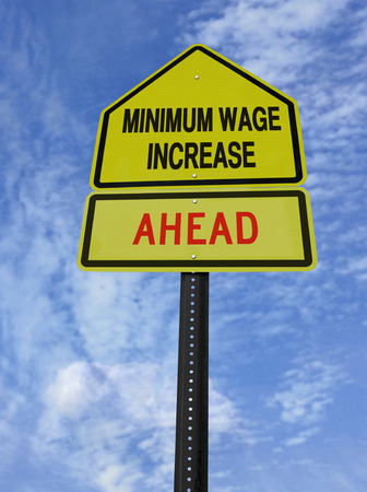 conceptual sign with words minimum wage increase  ahead over blue skyの写真素材