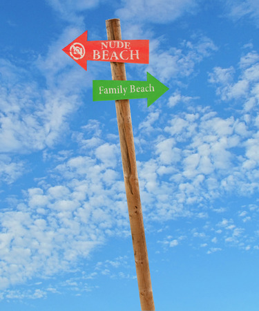 wooden arrow direction signs post to the nude and family beaches against a blue skyの写真素材