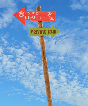 wooden arrow direction signs post to the nude and private beaches against a blue skyの写真素材