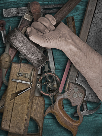 faded colors of a vintage woodworking tools and hand holding hammer on wooden benchの写真素材