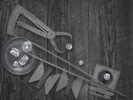 black and white image of a vintage jeweler tools and diamonds over wooden bench, space for textの写真素材