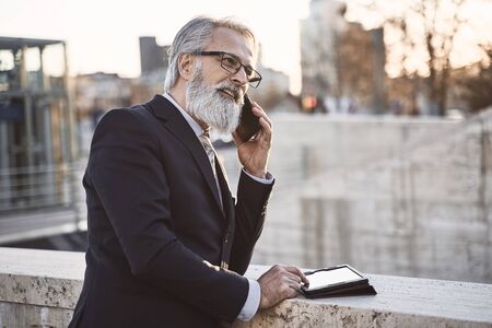 caucasian senior CEO using a smartphone and smart tablet in an urban environment, outdoor shot.の写真素材