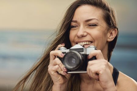 portrait of a beautiful brunette photographer taking a picture at the seasideの写真素材