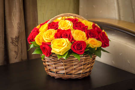 A bouquet of yellow and red roses in a basket on the table surface.の写真素材