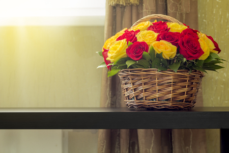 A bouquet of yellow and red roses in a basket on the table surface.の写真素材