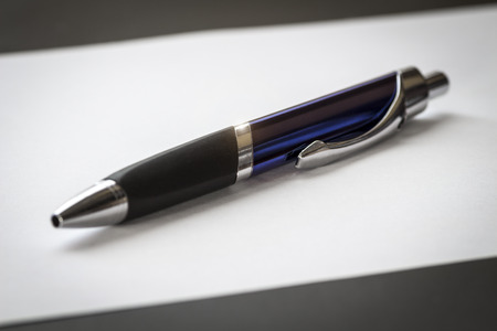 Office ballpoint pen lies on a sheet of paper close-up.