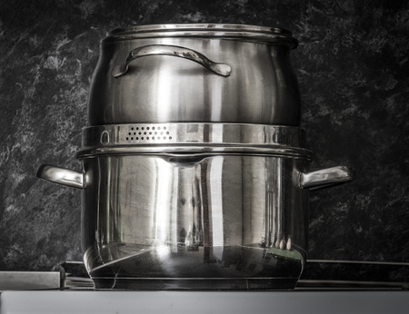 Stainless steel kitchenware on table, on dark background.