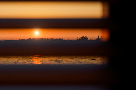 The setting sun shines through the closed horizontal blinds.