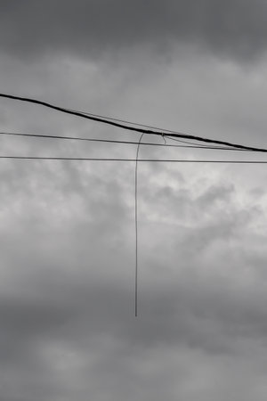 The broken end of an electrical wire hangs from a power line.の写真素材