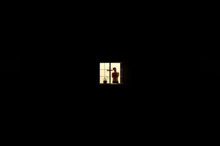 A man stands at an open window in his apartment.