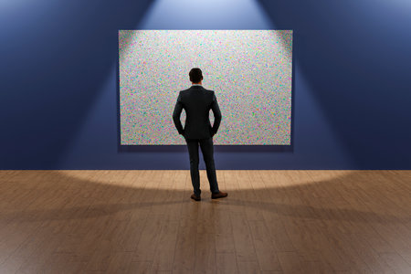 A man in an exhibition hall examines a painting hanging on the wall.の写真素材