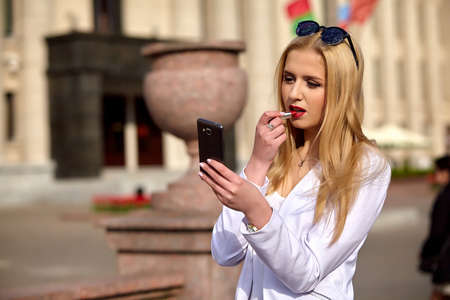 Young stylish woman applying lipstick  against summer urban background.の写真素材