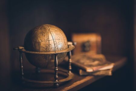 Antique copper globe, against a dark background, in the background a chest and booksの写真素材
