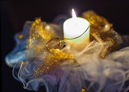 Wedding rings. Candle. Lace with gold embroidery. Light from a candle.の写真素材