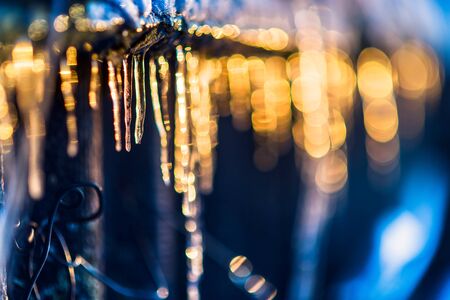 Beautiful icicles shine in sun. Spring landscape with ice icicles hanging from roof of house.