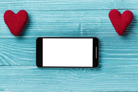 Smartphone with white screen and knitted heart on a beautiful blue wooden background. Valentine's day conceptの写真素材