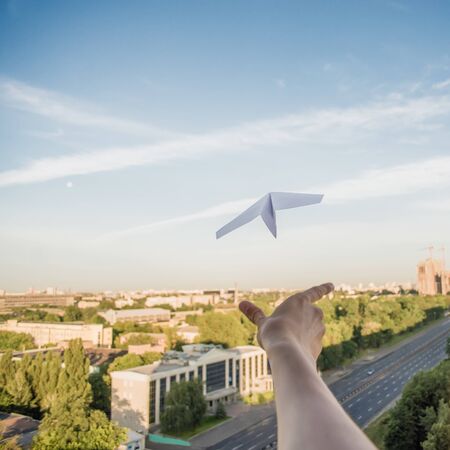 A man is launching a paper plane in the sky above the cityの写真素材
