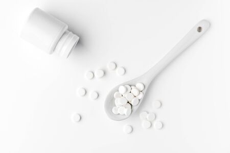 Pills on the spoon and scattered on the white surfaceの写真素材