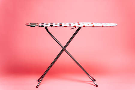 Pink, colorful ironing board stands in the center on a pink background. Homework concept.の写真素材