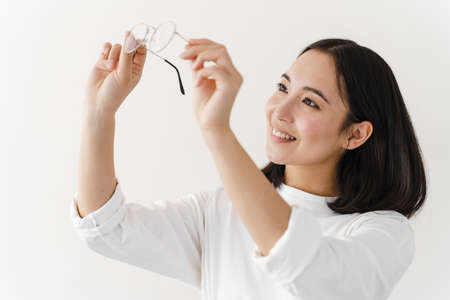 Beautiful woman checking the cleanliness of glasses. Girl posing on a white wall background.の写真素材