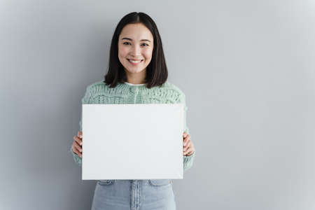 Young pretty woman smiles and holds blank piece of paper in her hands. Mock up. Copy space for your...