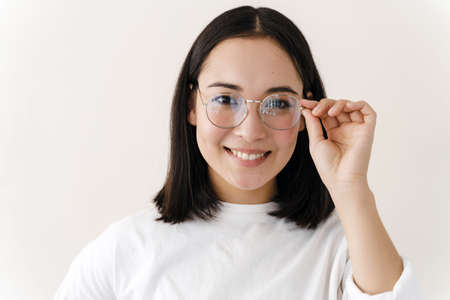 Young businesswoman adjusts her glasses and smiles. Girl isolated on white wall background.の写真素材