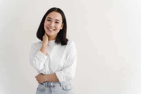 Portrait of modern woman smiling broadly at camera, standing against white background. Young girl...