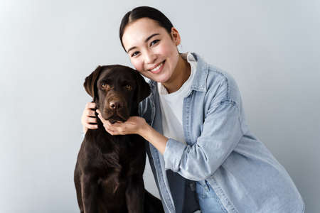 Loving woman stroking her pet on a gray wall background. Concept - faithful friend of man dog.の写真素材