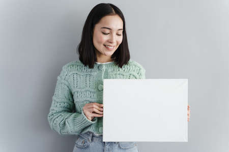 Pretty woman looks at a piece of paper in her hand. Girl on a background of a gray wall. copy space, place for text, advertisingの写真素材