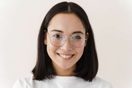 Attractive girl with glasses looks straight into the camera. Young woman posing on a white wall...