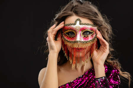 Beautiful woman wearing venetian carnival mask against black background. Holds hands near face - Imageの写真素材