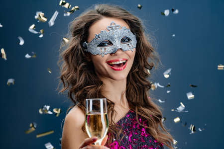 Happy woman wearing venetian  carnival mask at party over holiday background with tinsel. Raising glass of champagneの写真素材