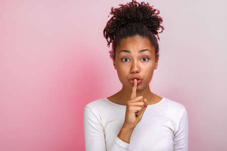 Cute mulatto woman shows a silence gesture touching by index finger her lips. Concept gesture - Imageの写真素材