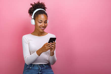 Portrait of a mulatto girl in earphones and holding a mobile phone looking at the screen - Image