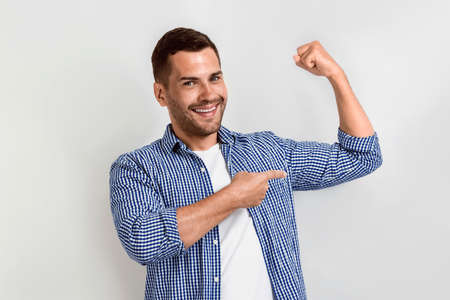 Happy man laughing and pointing for his biceps by his arm.- Imageの写真素材