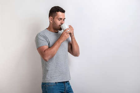 Man stands with cup of morning tea or coffee and drinking it with pleasure.- Imageの写真素材